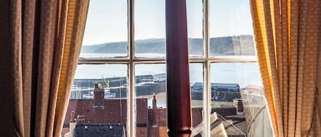 A room with a large window, curtains, and a wooden bedpost.