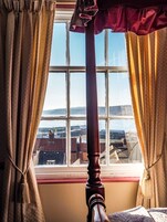 Quarto com uma grande janela, cortinas e um poste de cama de madeira.
