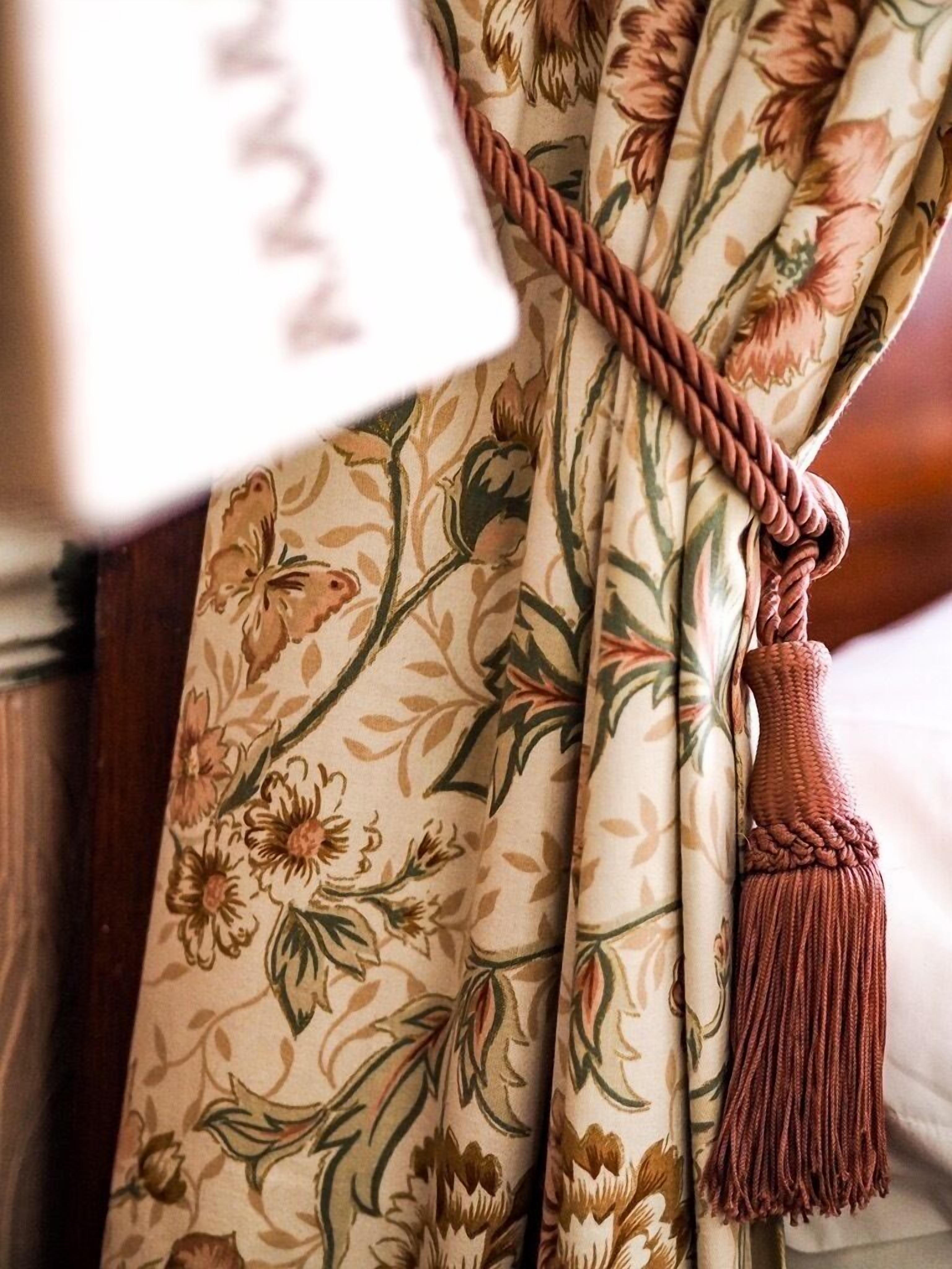 A curtain with a floral pattern and a tassel.