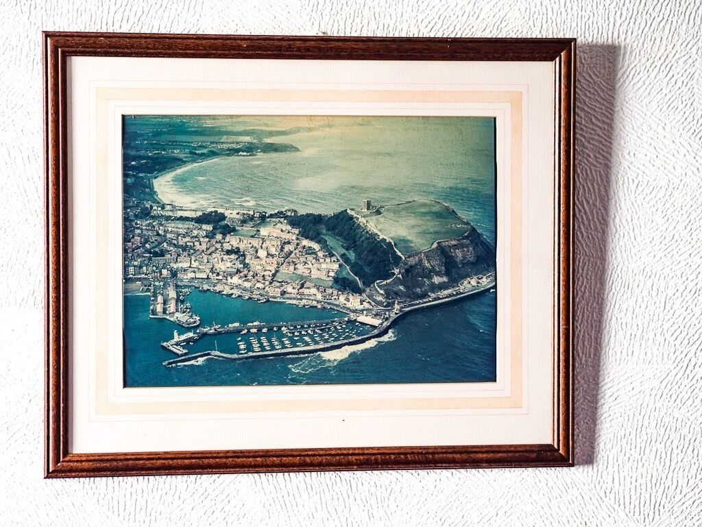 Une photographie aérienne encadrée d’une ville côtière, avec un port, des bâtiments et un phare imposant.