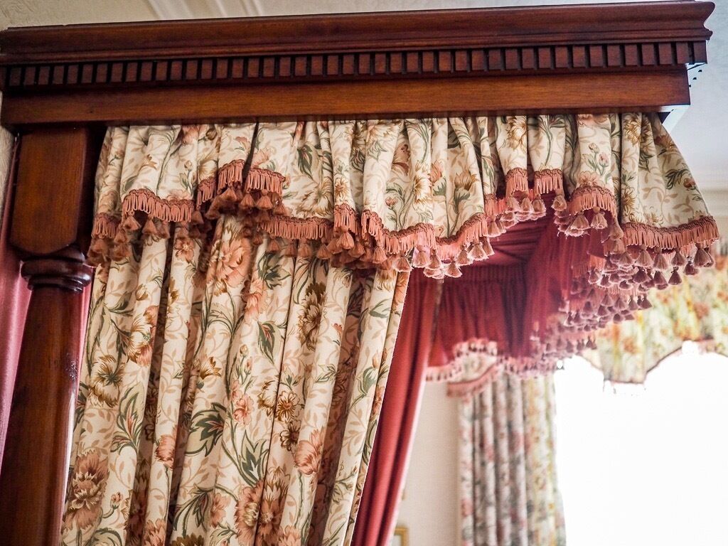 Una habitación con estructura de cama de madera y cortinas de estampado floral con flecos.