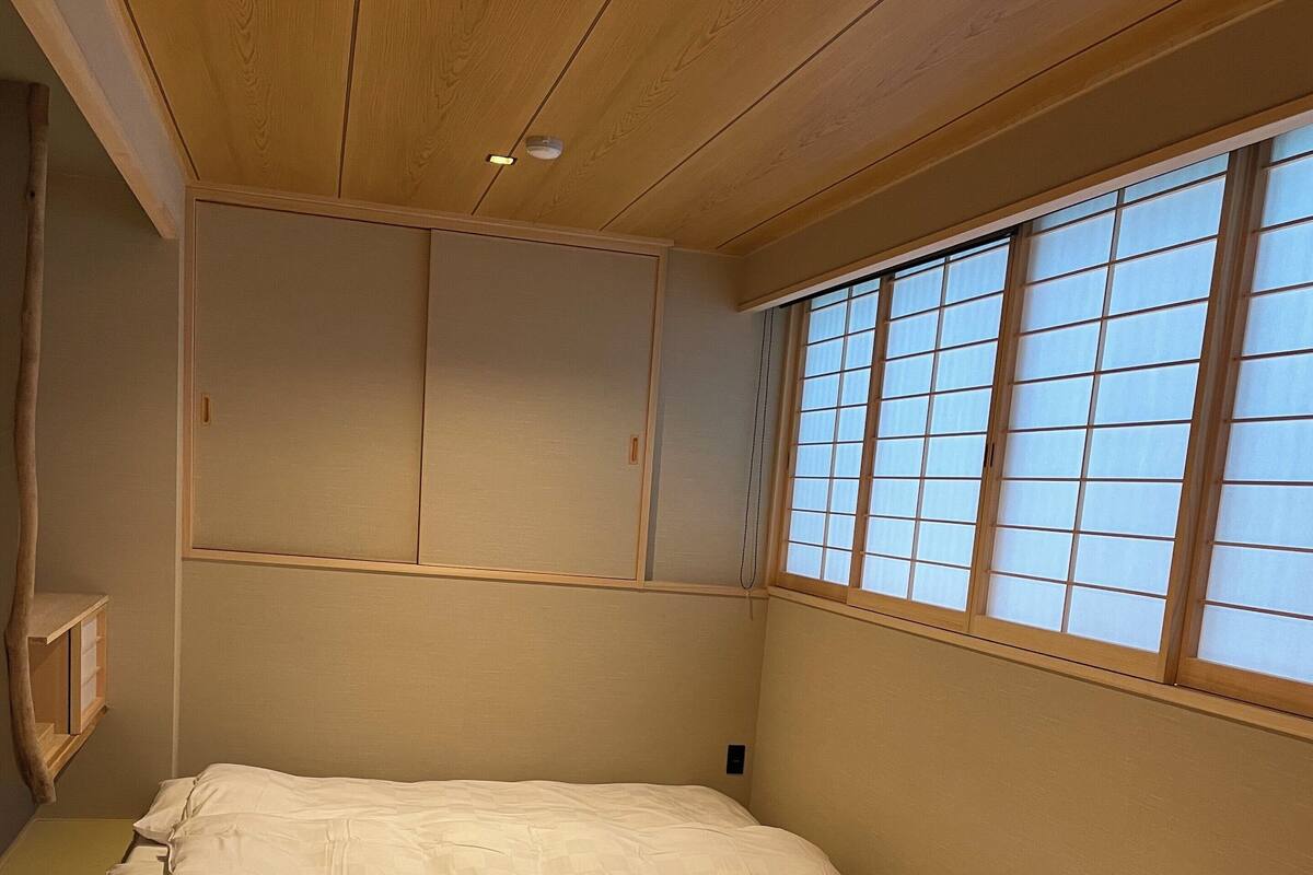A room with a large bed, wooden ceiling, sliding doors, and a window with grid panes.