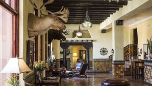 Un vestíbulo con una gran cabeza de venado montada en la pared, muebles de madera, una araña y un suelo de baldosas.