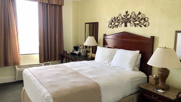 Une chambre d’hôtel avec un grand lit, deux lampes de chevet, un bureau avec une chaise, une fenêtre avec des rideaux et un élément décoratif mural.