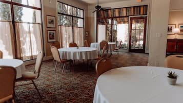 A dining area with round tables and chairs, large windows, and a ceiling fan.