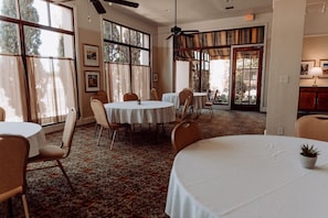 Un área de comedor con mesas y sillas redondas, ventanas amplias y un ventilador de techo.