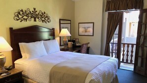 Une chambre d’hôtel avec un grand lit, deux tables de chevet, une lampe, une chaise, un bureau, une fenêtre avec des rideaux et un élément décoratif mural.