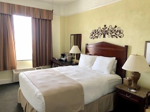 A hotel room with a large bed, a desk with a chair, a desk lamp, and a decorative wall piece. - Hotel EL Capitan (Van Horn)