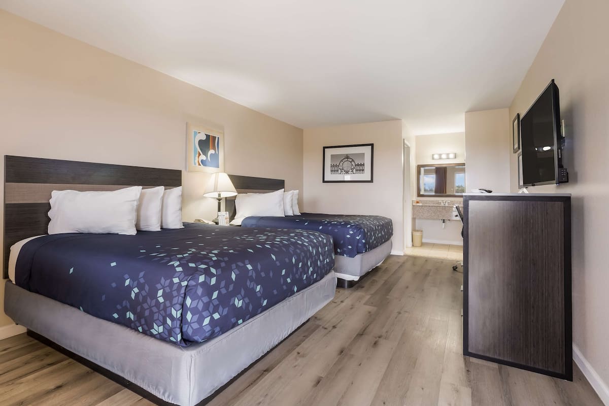 Habitación de hotel con dos camas, un escritorio, un televisor y un baño a la vista.