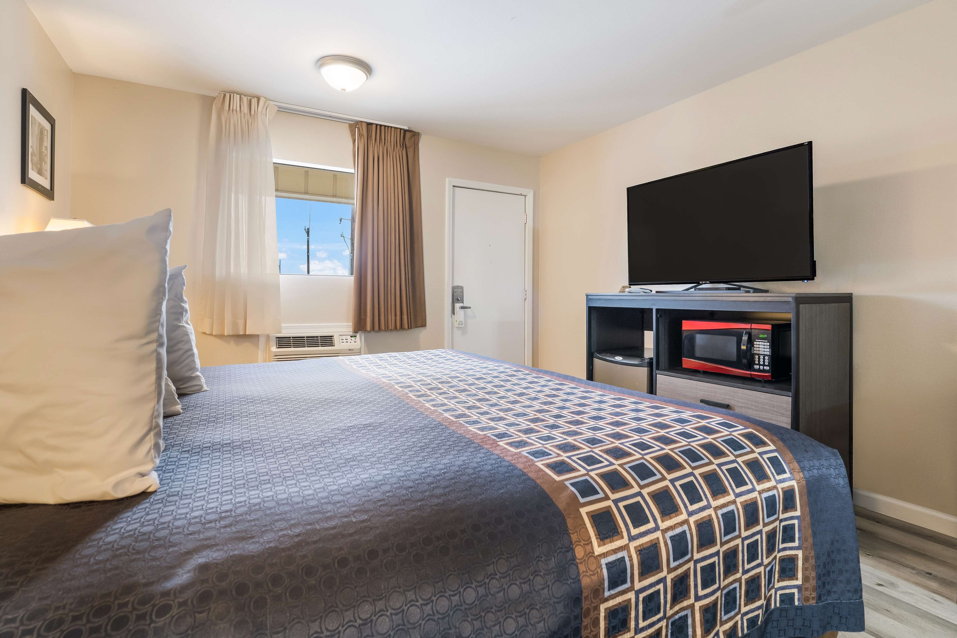 Habitación de hotel con cama, televisión de pantalla plana, microondas y ventana con cortinas.
