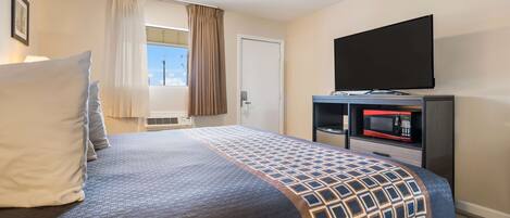 A hotel room with a bed, a flat-screen TV, a microwave, and a window with curtains.