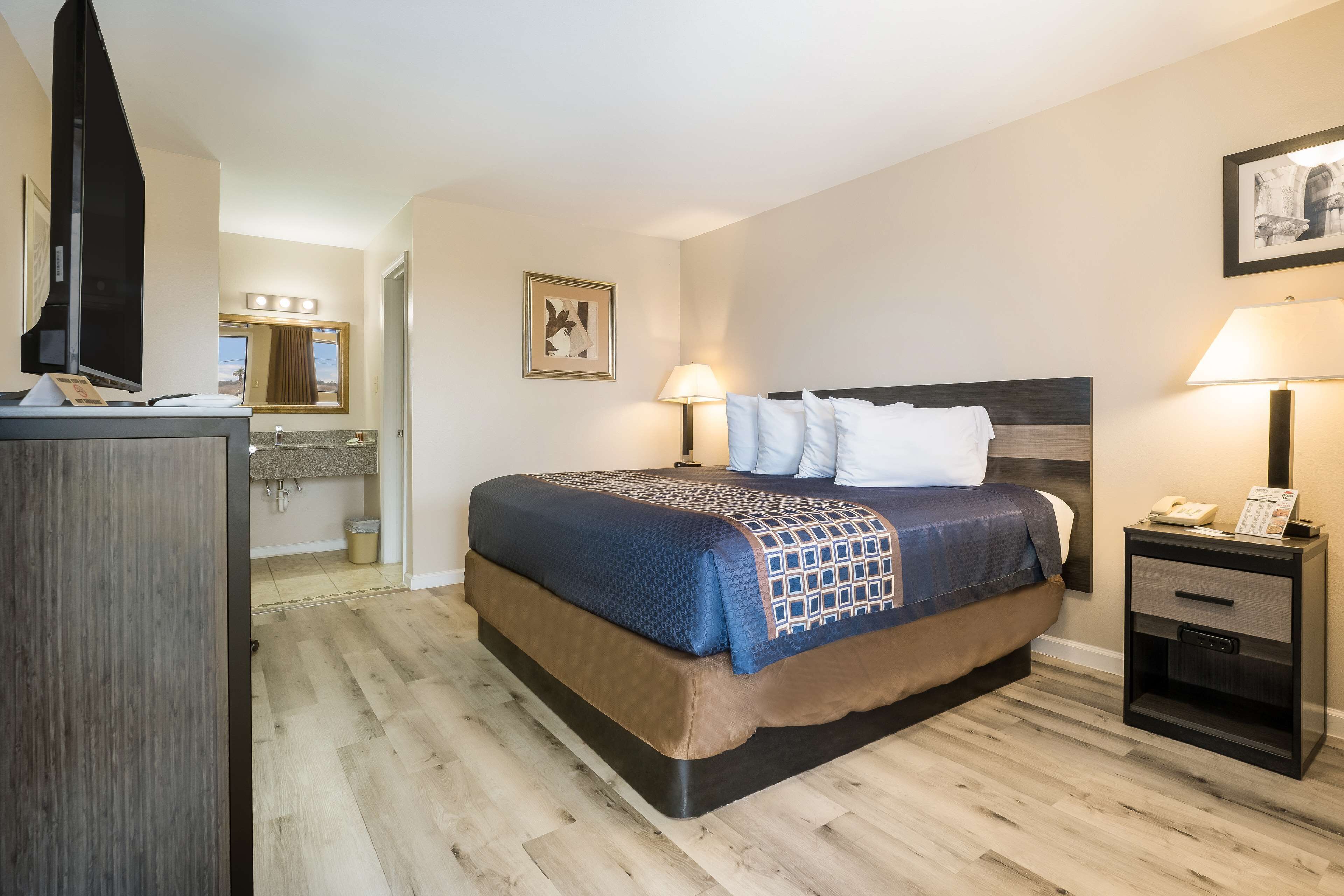 Une chambre d’hôtel avec un lit, une table de chevet, une lampe et un téléviseur posé sur un meuble.