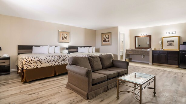 Habitación de hotel con cama, sofá, mesita de vidrio, tocador con espejo y lavamanos.