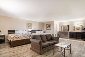 Habitación de hotel con cama, sofá, mesita de vidrio, tocador con espejo y lavamanos.