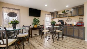 Un comedor con mesa de vidrio y sillas de metal, una cocina con armarios de madera y un microondas, y plantas en macetas.