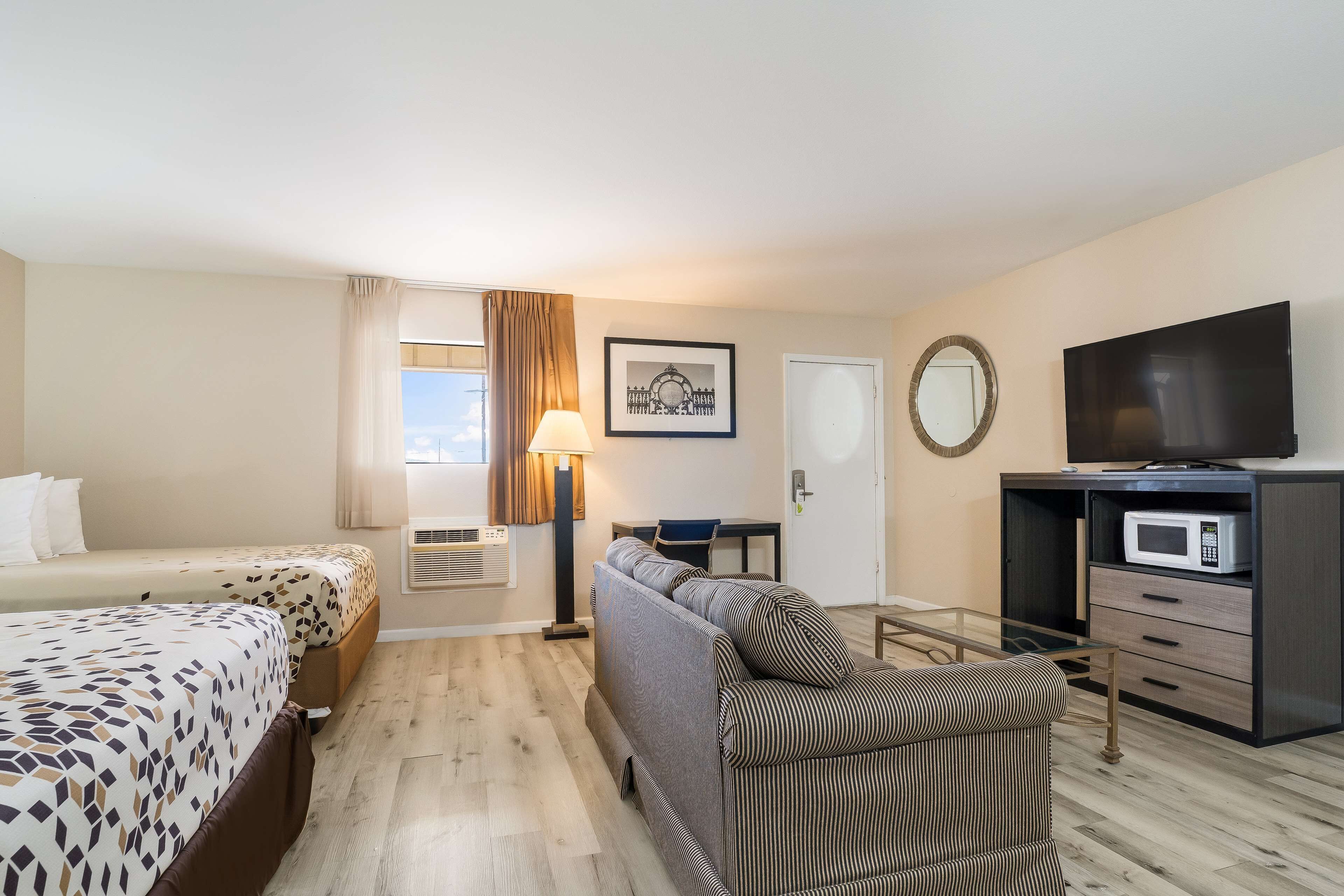 Habitación de hotel con dos camas, un sofá, televisión, microondas y escritorio con lámpara.