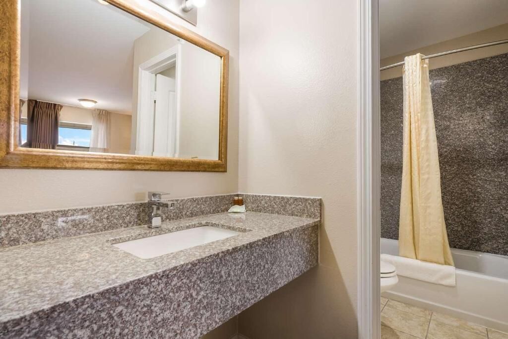 A bathroom with a granite countertop, a sink, a mirror, and a shower with a curtain.