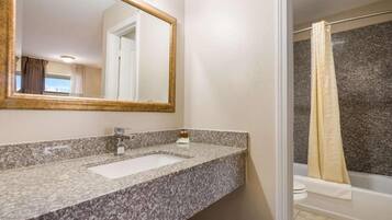 Un baño con encimera de granito, lavamanos, espejo y ducha con cortina.