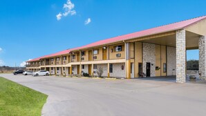 Un motel con techo rojo y fachada de piedra, que cuenta con un estacionamiento con varios autos.
