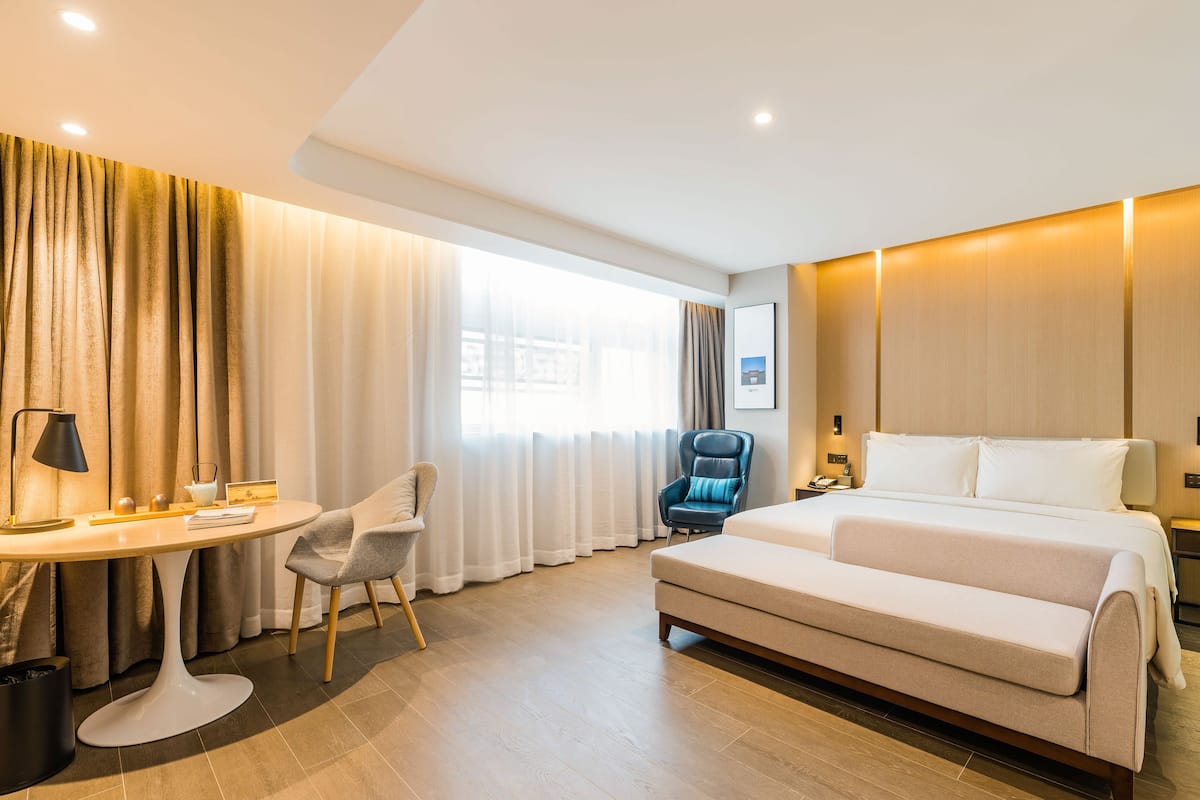 Habitación de hotel con cama, escritorio con silla, lámpara y ventana con cortinas.