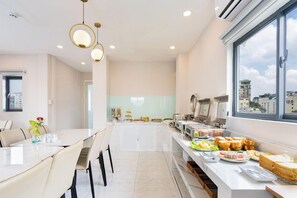 Un comedor moderno de hotel con una barra de buffet, un ventanal con vistas a la ciudad e iluminación contemporánea.