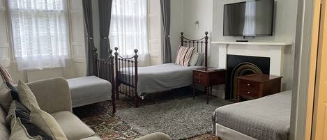 Ett hotellrum med två separata sängar, en soffa, en TV och en öppen spis.