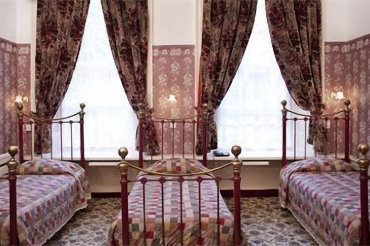A room with two beds, a window with curtains, and a patterned carpet.