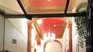 A hallway with a red carpet, ornate ceiling, and a chandelier. There are chairs and a table with a potted plant. - Atlas Guest House (Edinburgh)