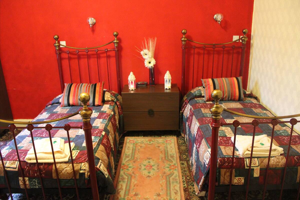 A room with two beds, a wooden dresser, and a red wall.