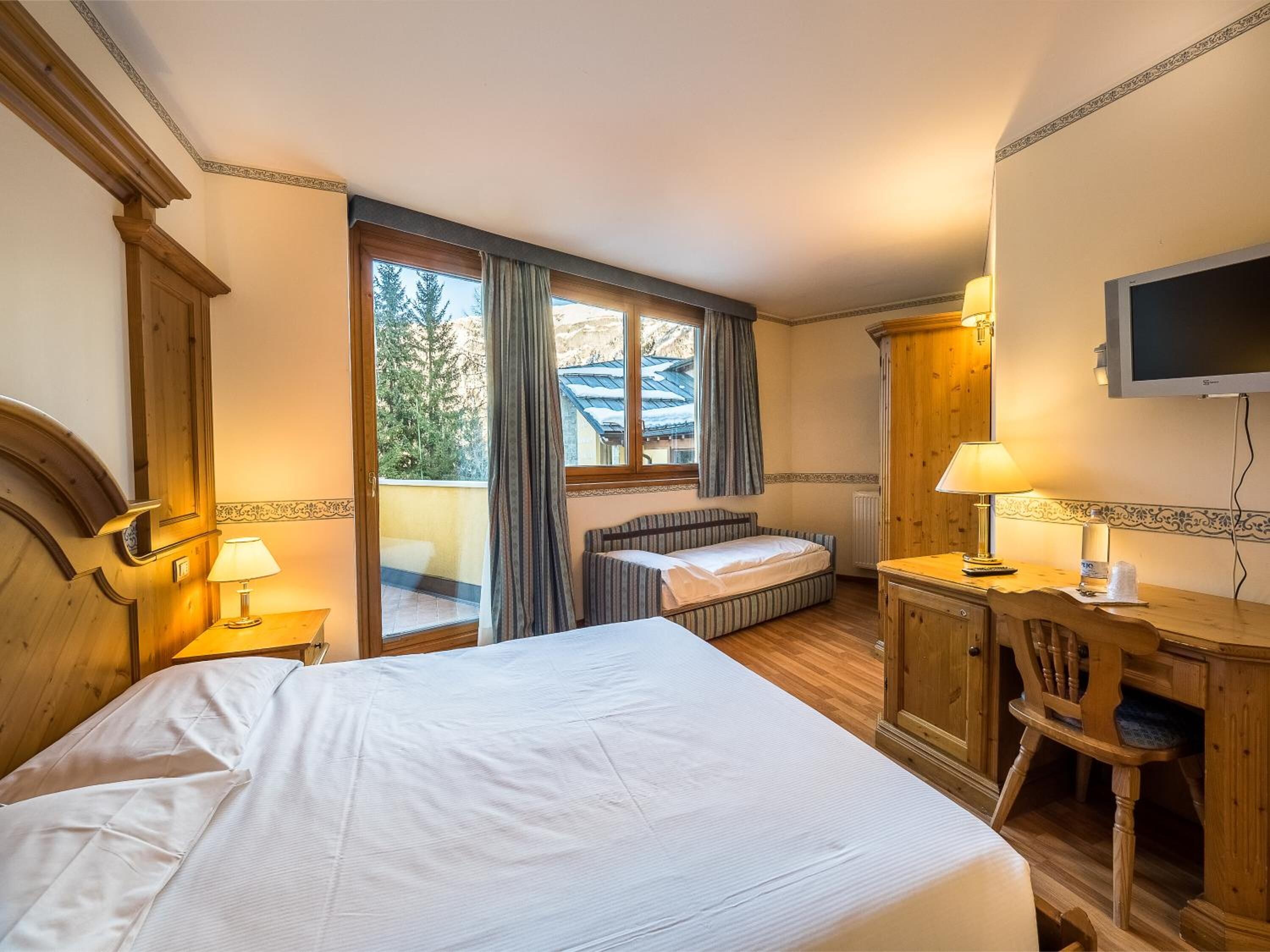 A hotel room with a large bed, a desk with a chair, a television, and a window with curtains.