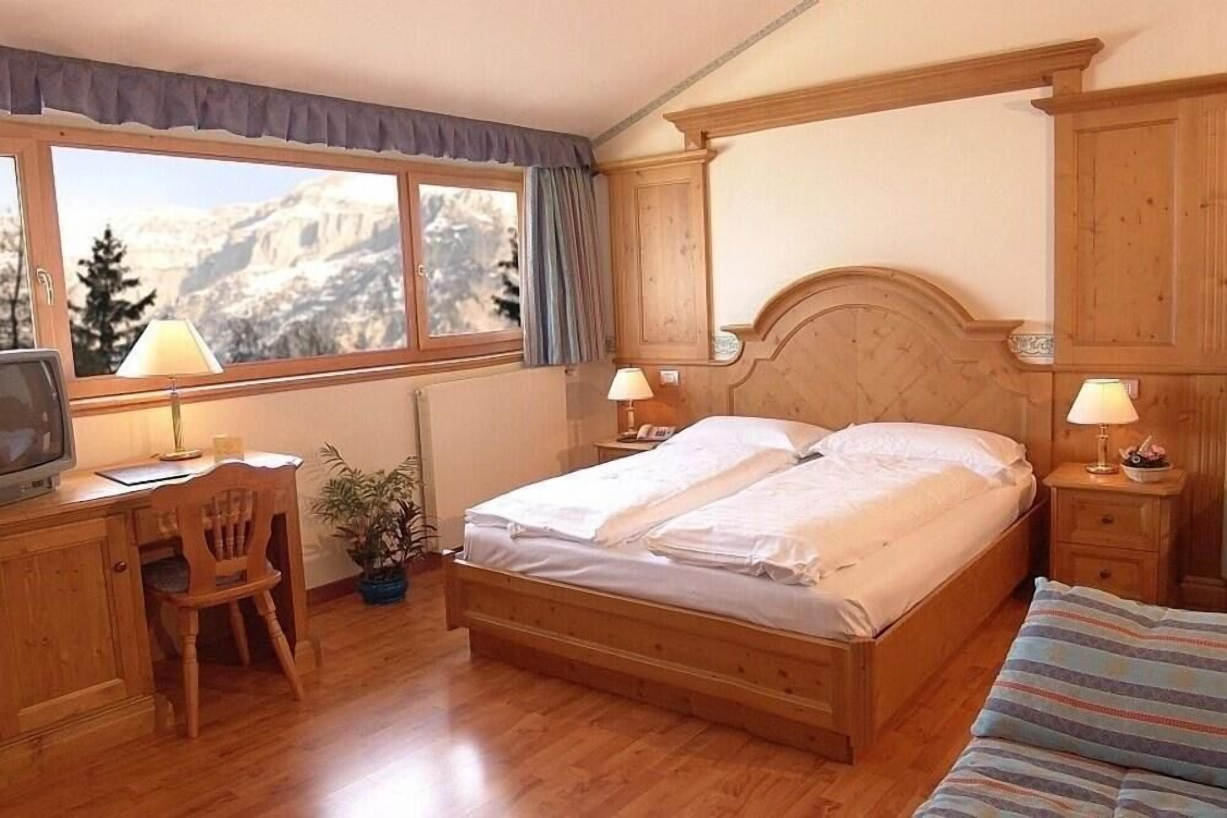 Un dormitorio con cama de madera, un escritorio con silla, un televisor y una ventana con vistas a la montaña.