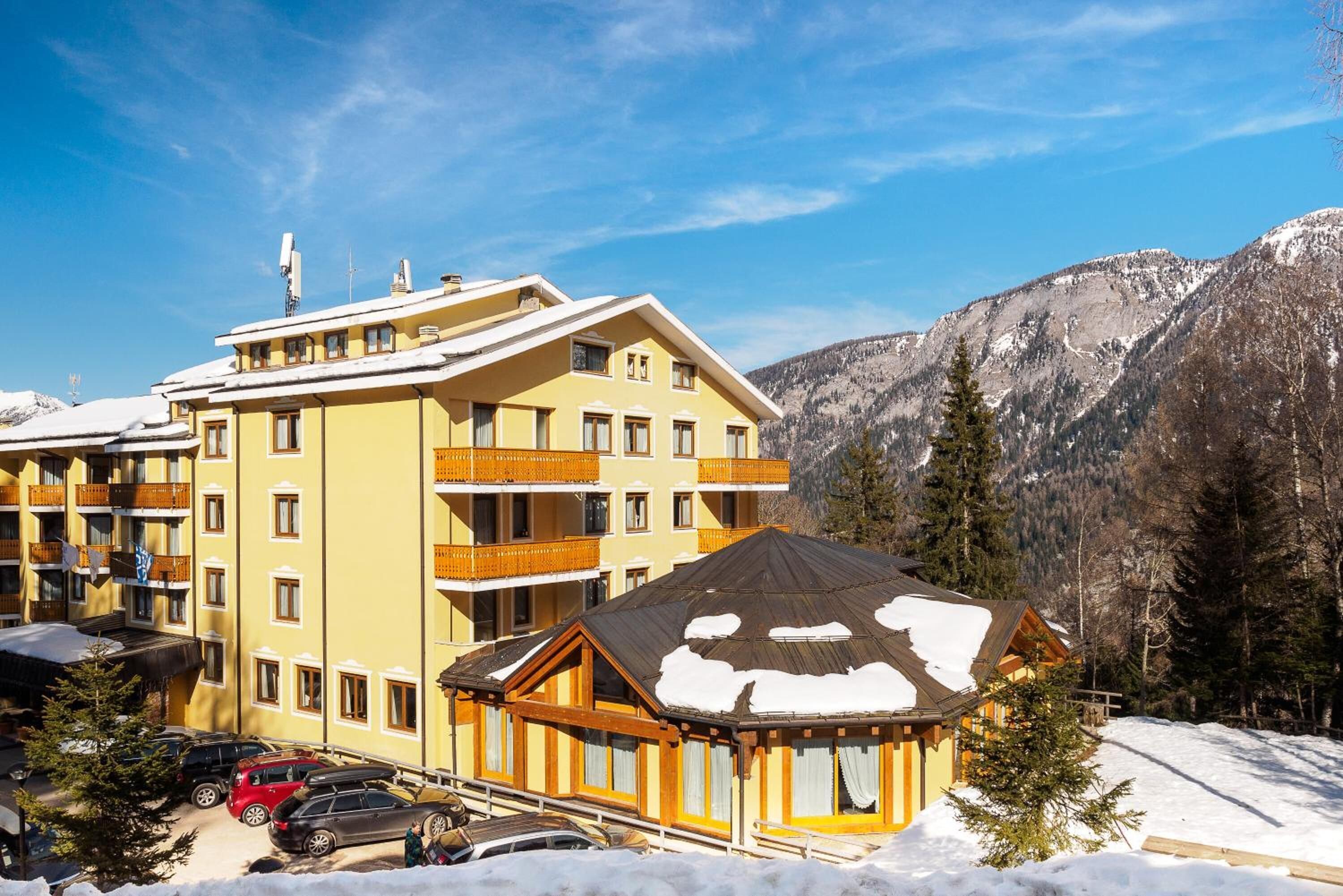 Un hotel de varios pisos con balcones, un albergue de esquí y montañas al fondo.