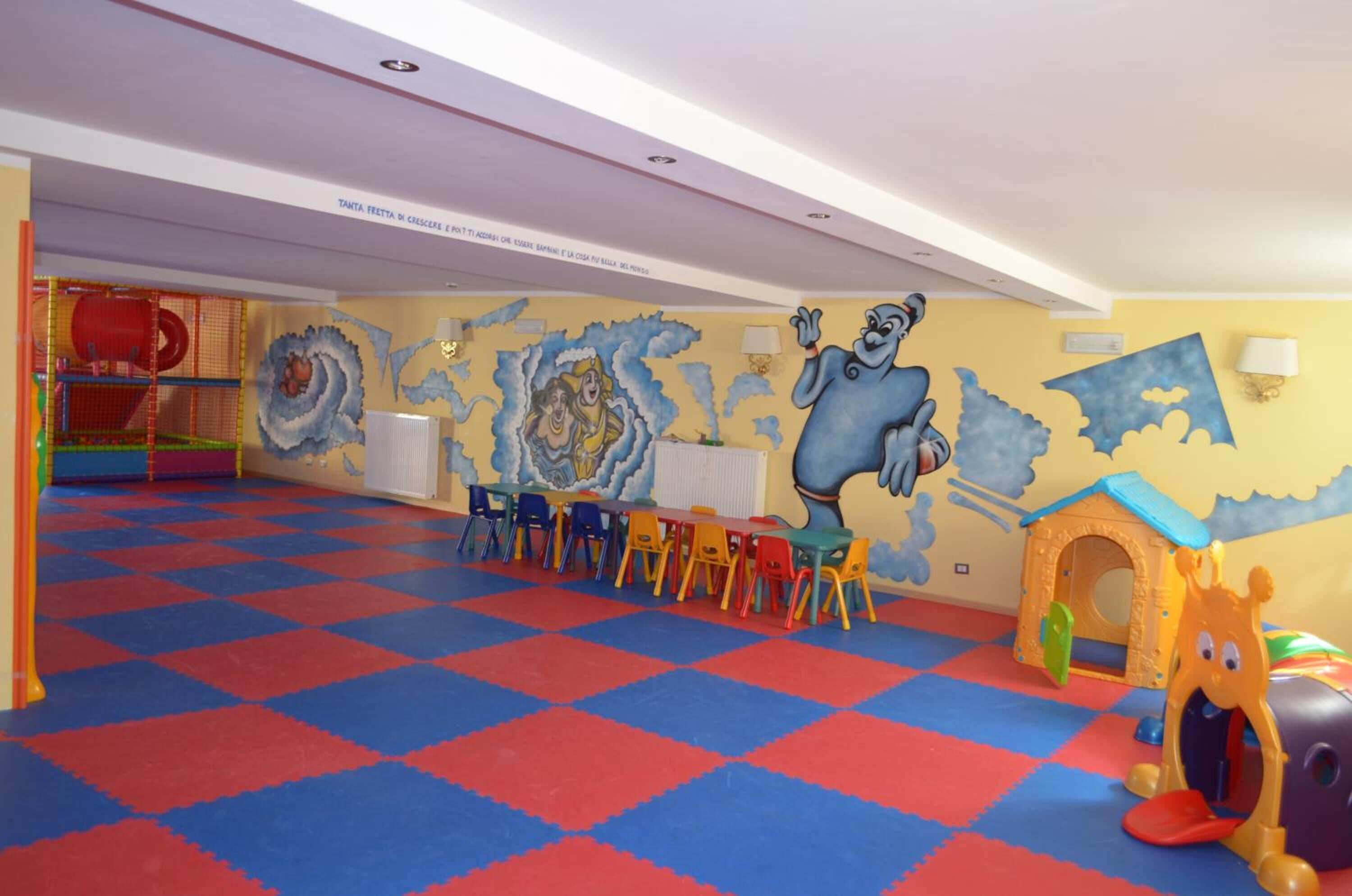 A children's play area with colorful mats, a slide, and a mural with cartoon characters.
