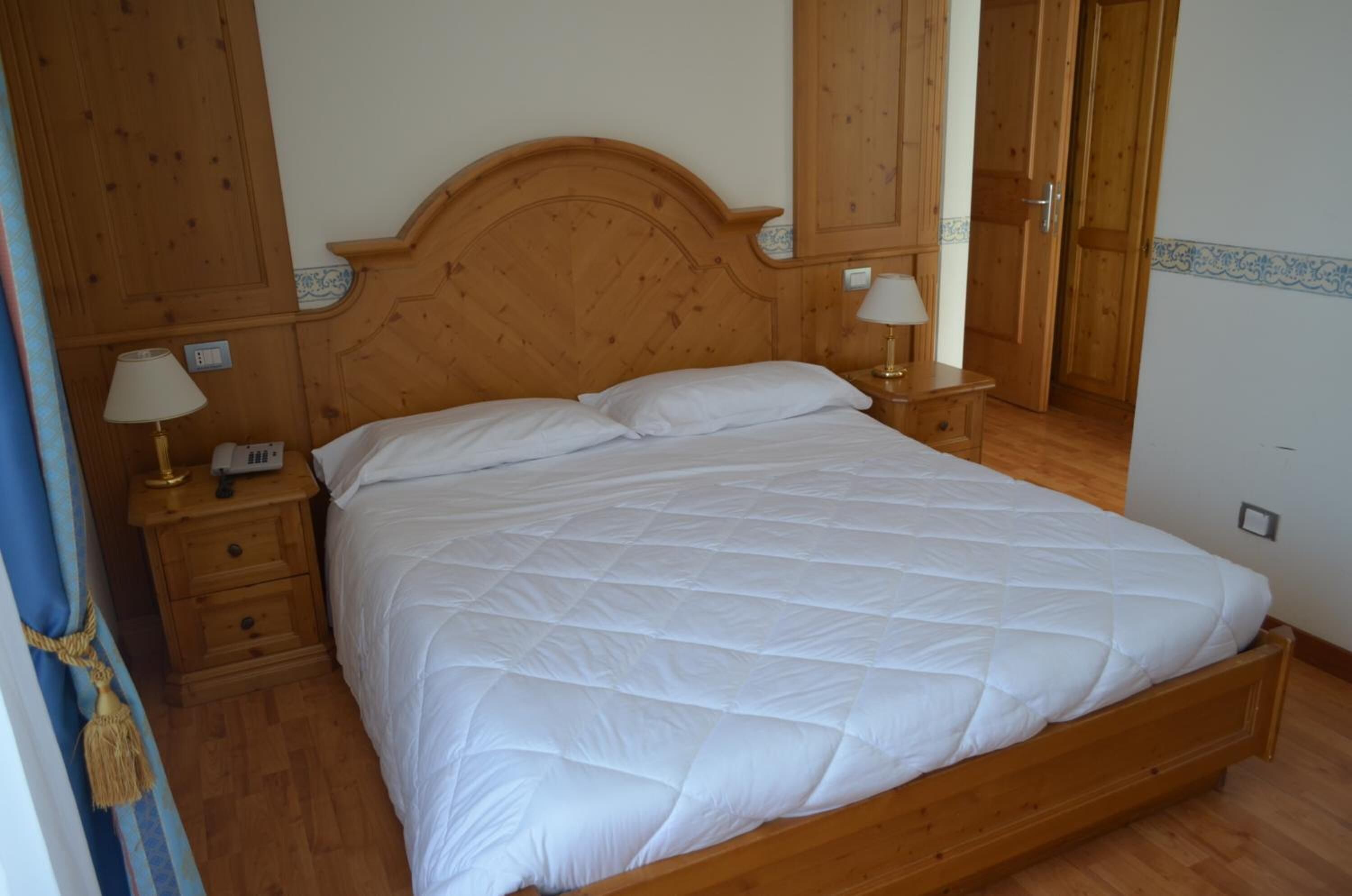 A neatly made bed with a wooden headboard, two bedside tables with lamps, and a wooden wardrobe.