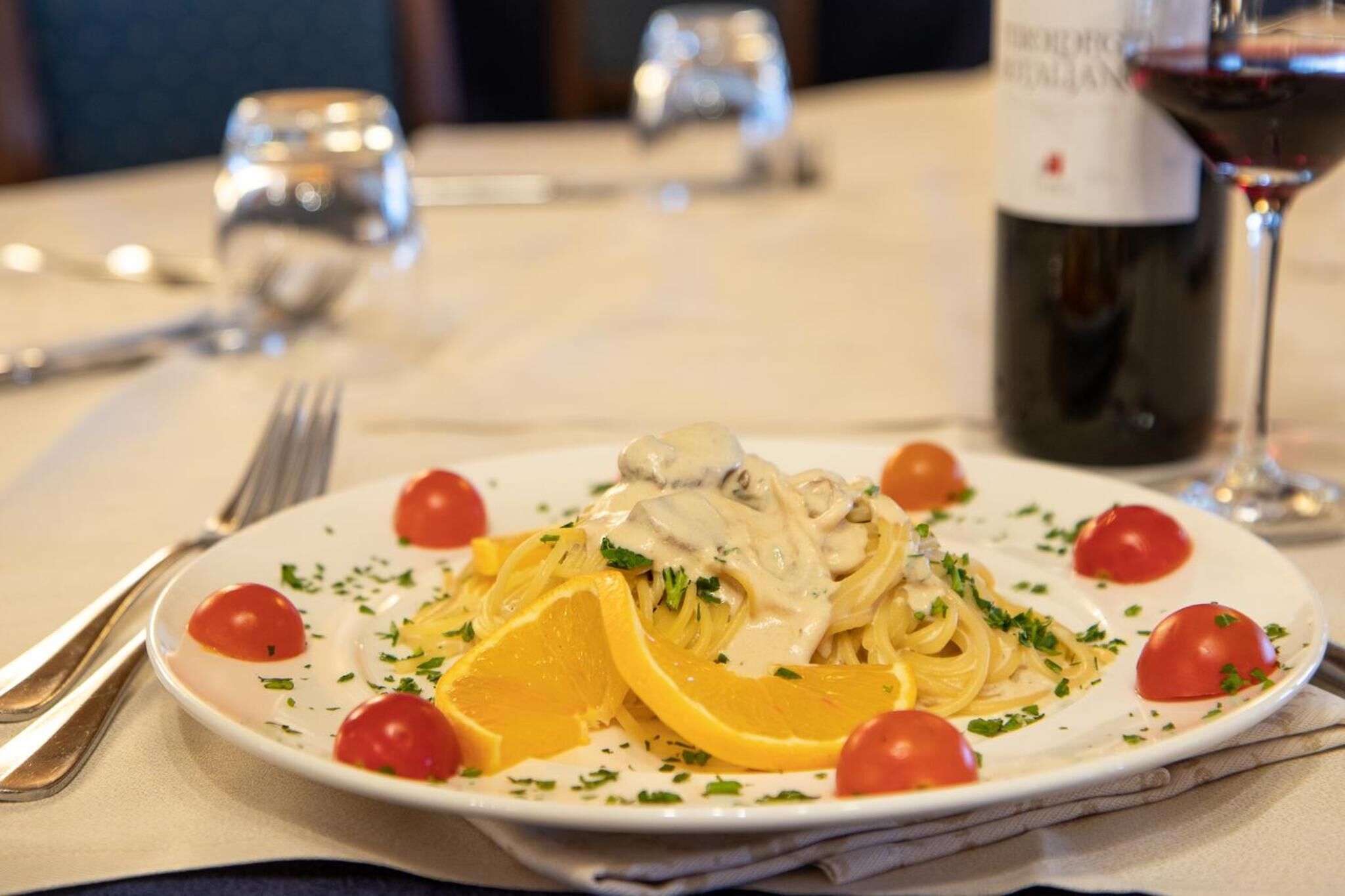 A plate of pasta with cherry tomatoes and orange slices on a table.