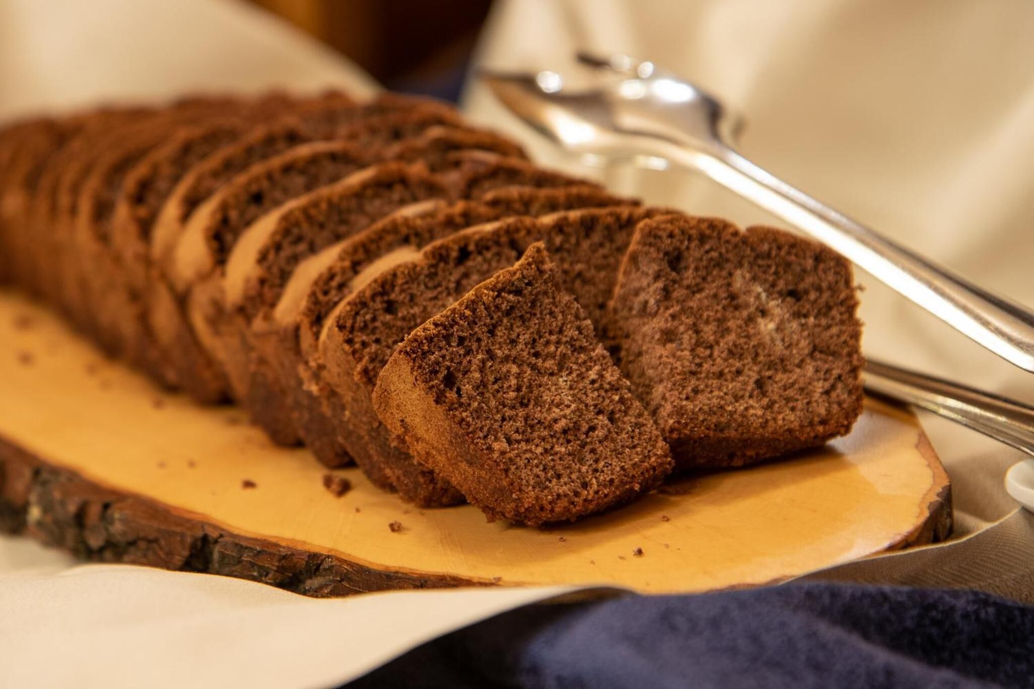 A loaf of dark brown bread sliced on a wooden board.