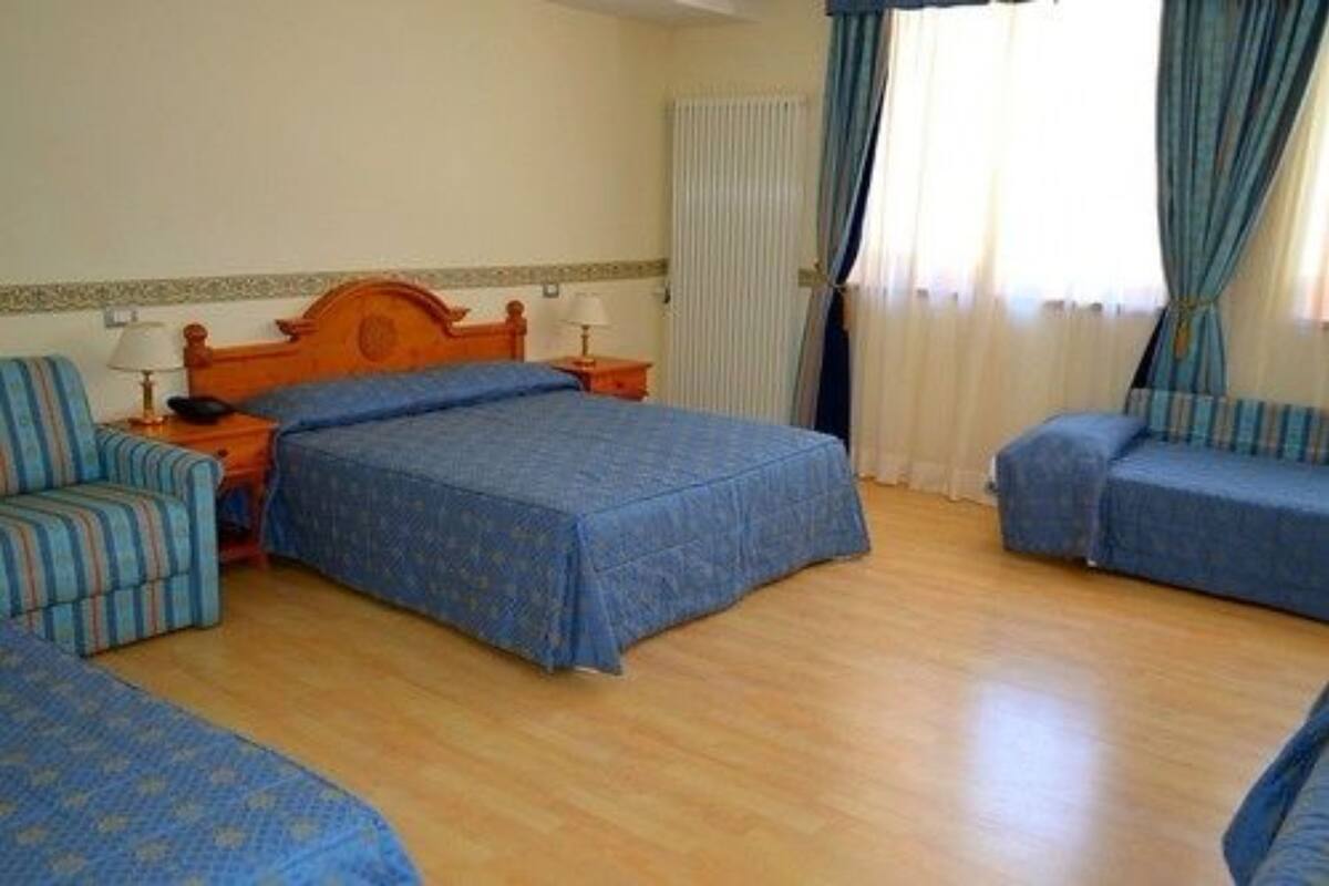Una habitación de hotel con dos camas individuales, un cabecero de madera, una mesita de noche con lámpara y una silla.