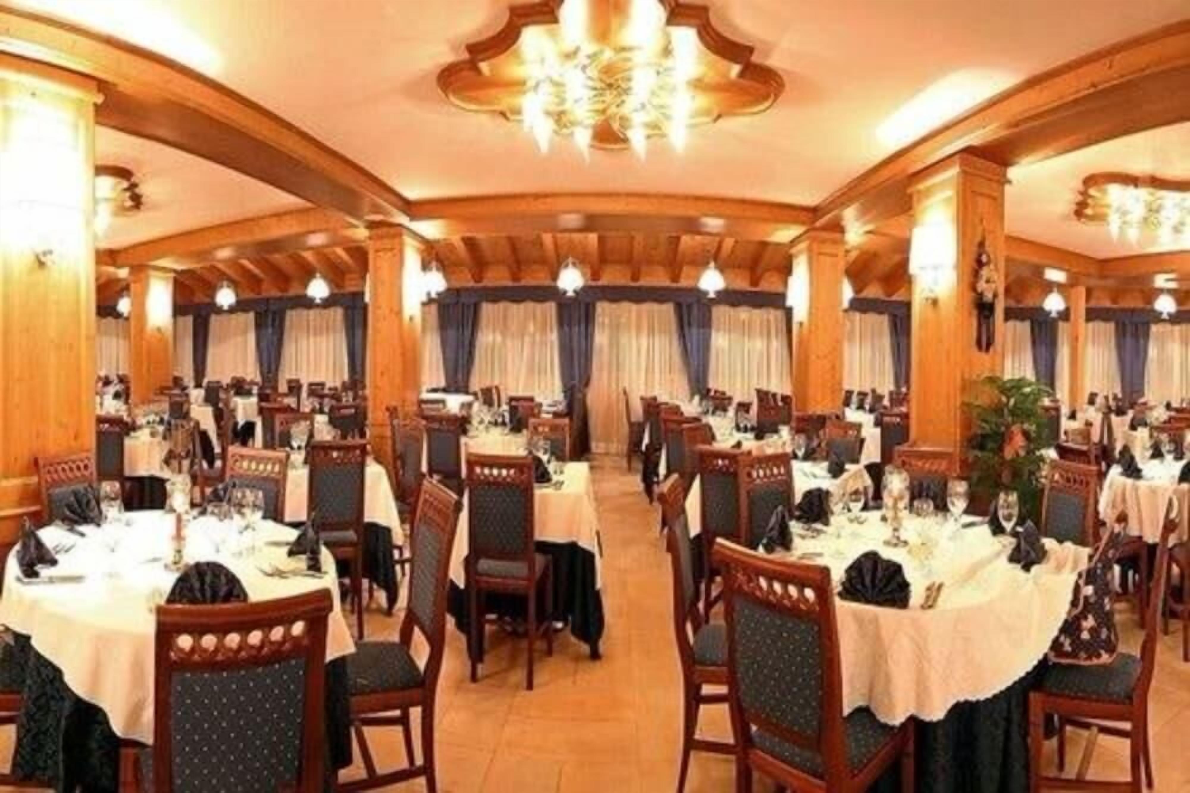 A formal dining room with round tables, wooden chairs, and chandeliers.