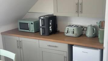 Une petite cuisine équipée comprenant un micro-ondes, un grille-pain et une bouilloire sur le plan de travail, un petit réfrigérateur et des placards de couleur claire.
