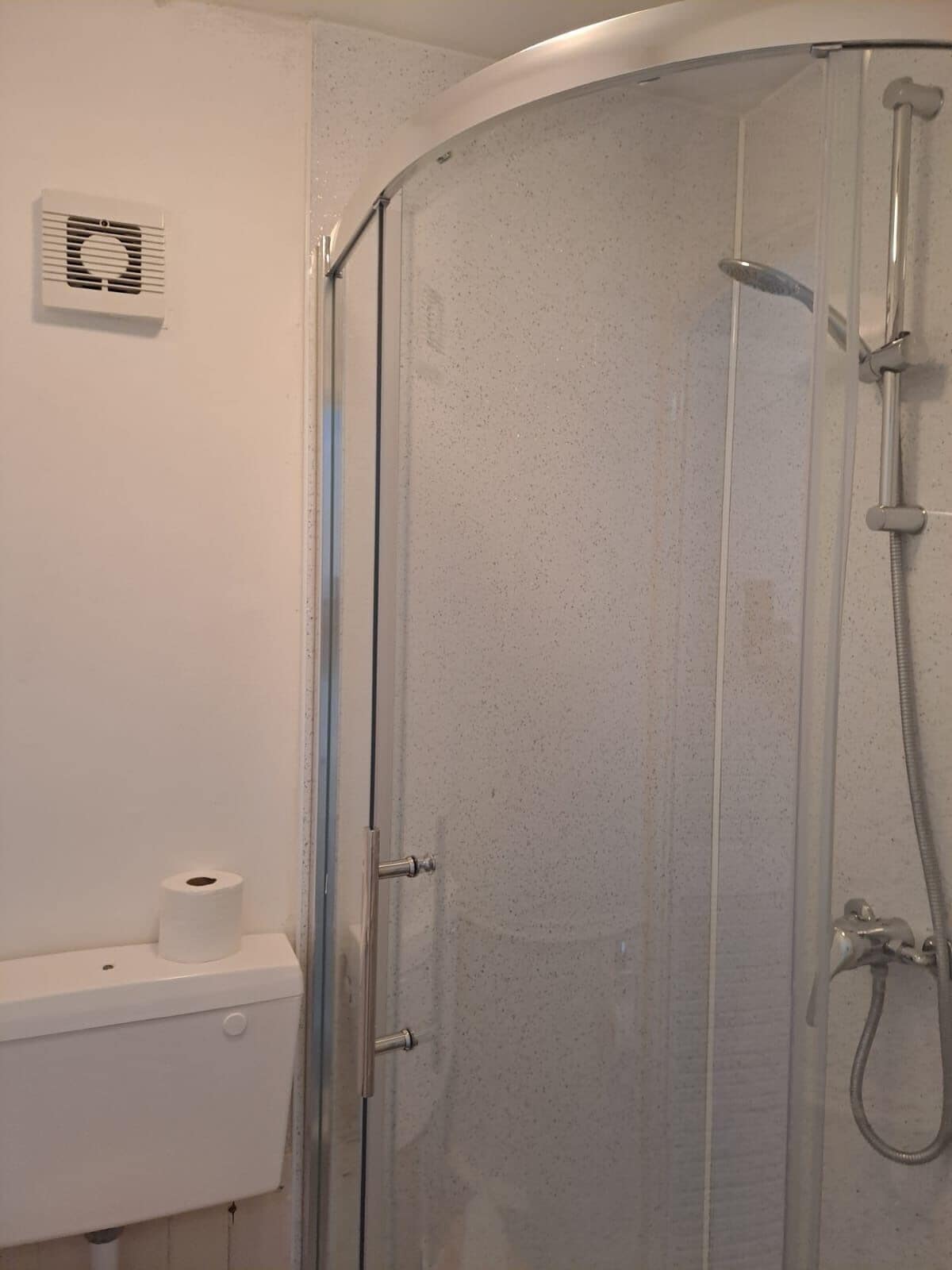 A shower enclosure with a glass door, a handheld showerhead, and a toilet paper roll on the wall.