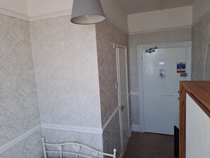 A hallway with patterned wallpaper, a white door with a fire action sign, and a white metal bed frame.