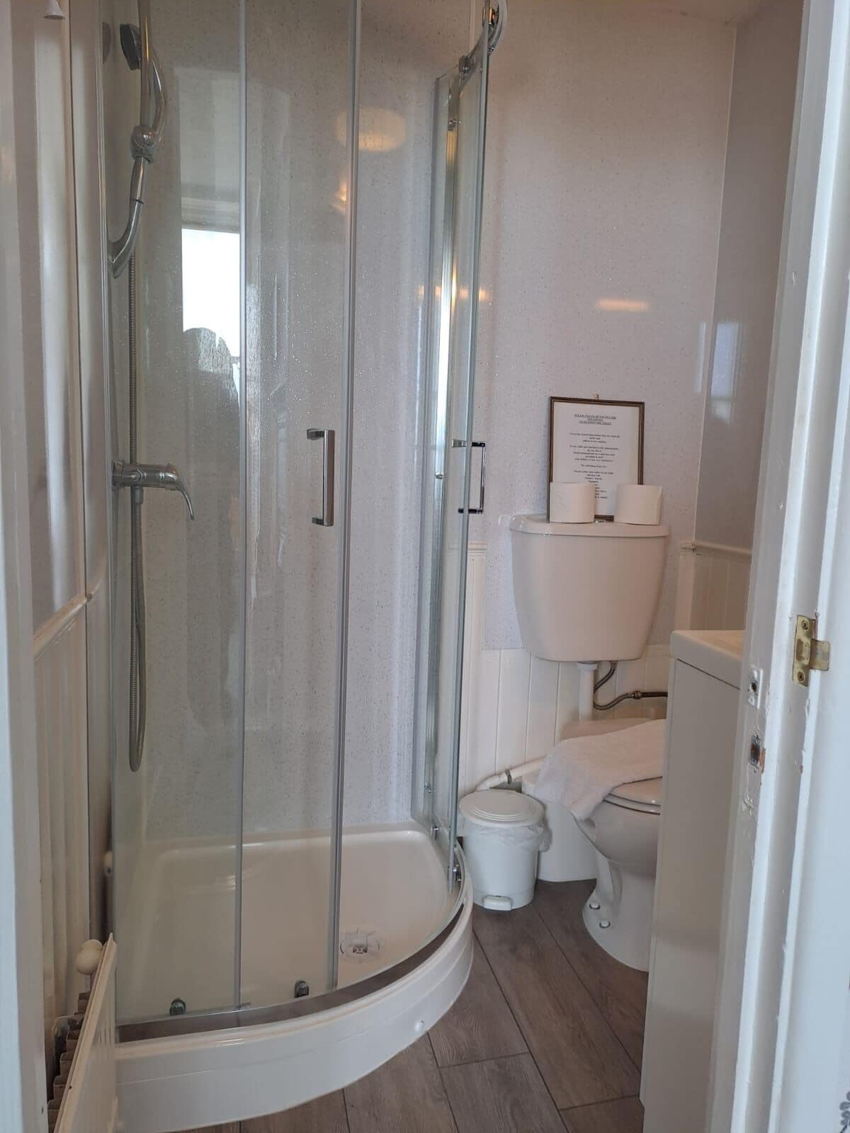 A bathroom with a glass-enclosed shower, a toilet, and a framed informational sign on the wall.