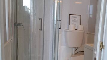 A bathroom with a glass-enclosed shower, a toilet, and a framed informational sign on the wall.