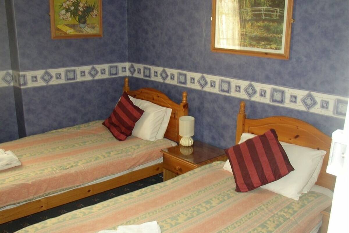 Two single beds with wooden headboards, a nightstand with a lamp, and a decorative border on the wall.