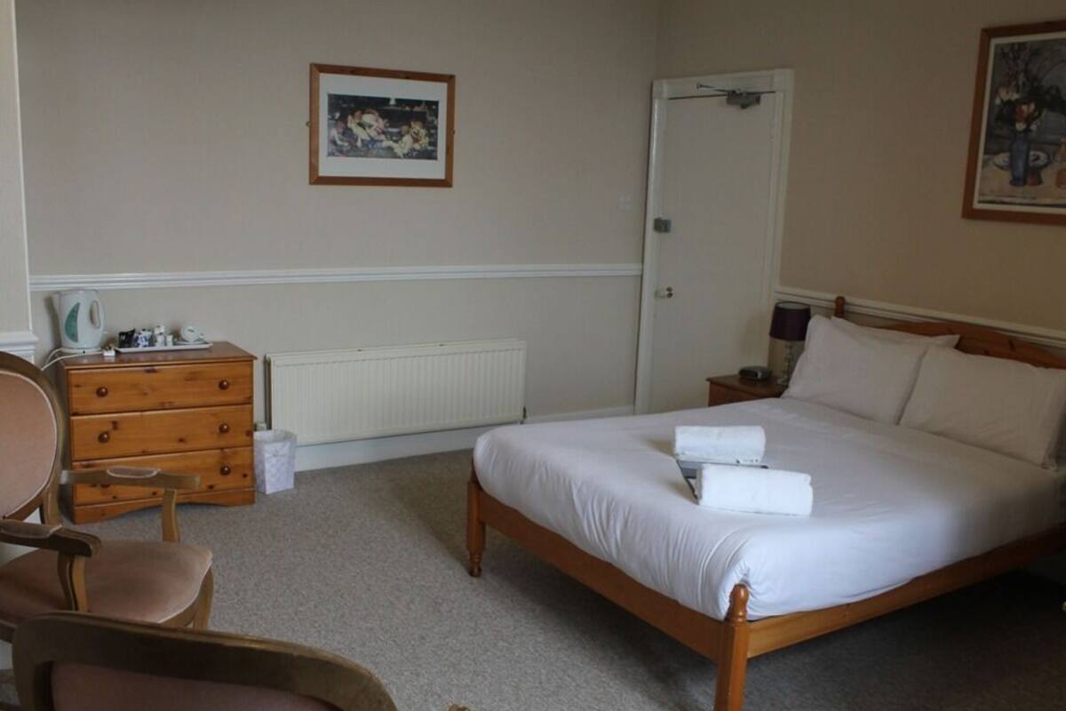 A bedroom with a wooden bed, a dresser, a chair, and a radiator.