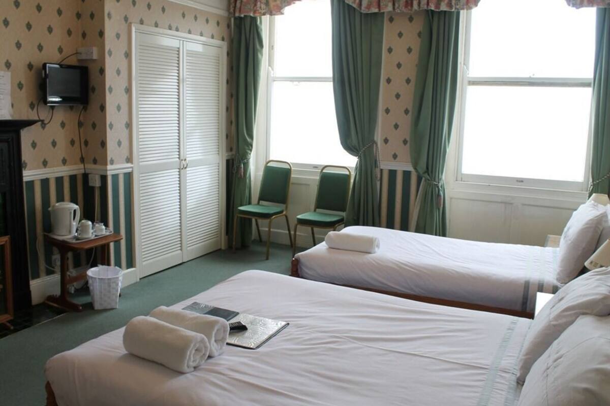 A hotel room with two beds, a television, a desk with a kettle, and a window with curtains.
