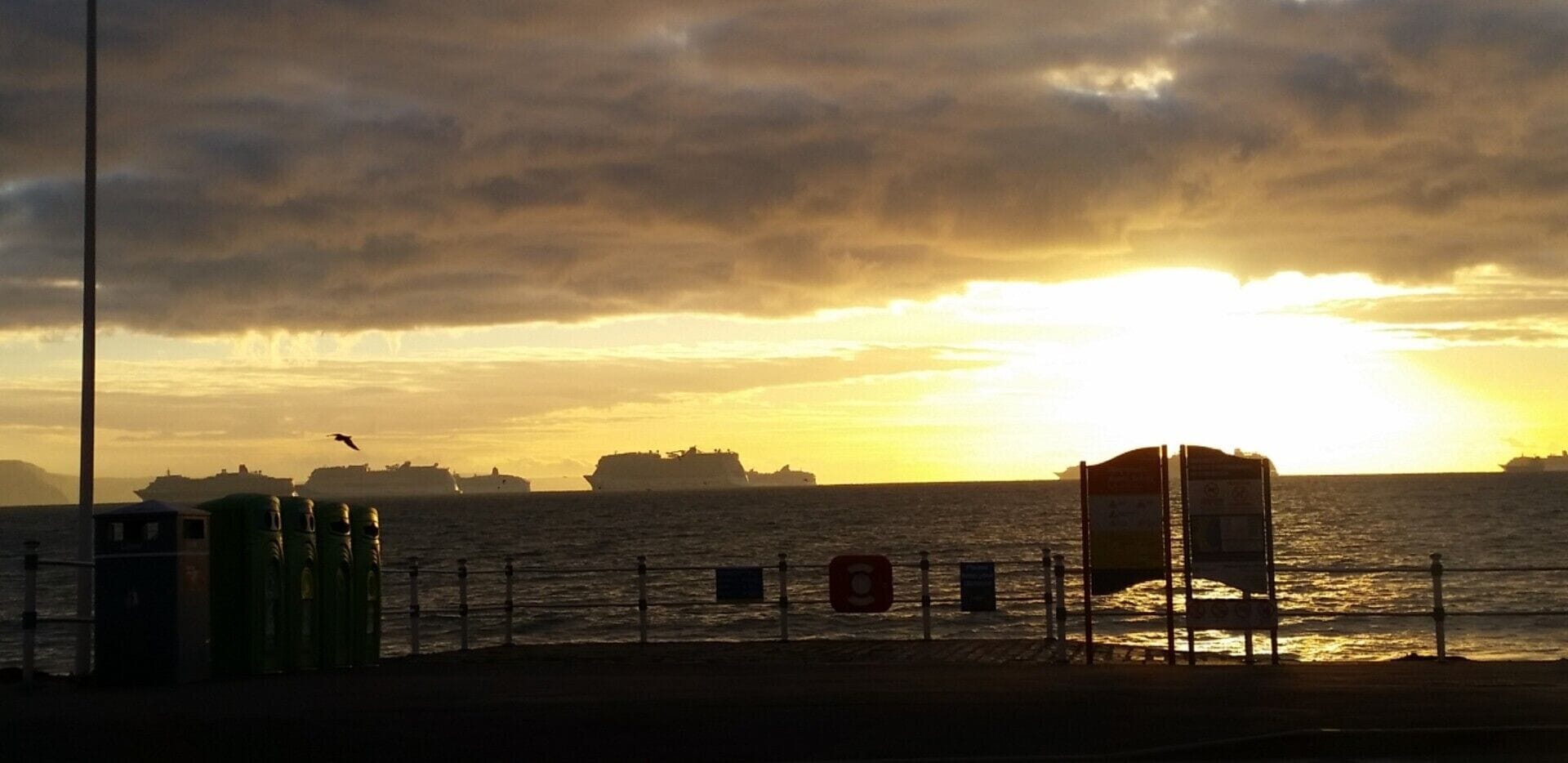 A sunset over the ocean with ships in the distance and a lifeguard tower on the shore.