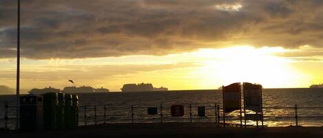 A sunset over the ocean with ships in the distance and a lifeguard tower on the shore.