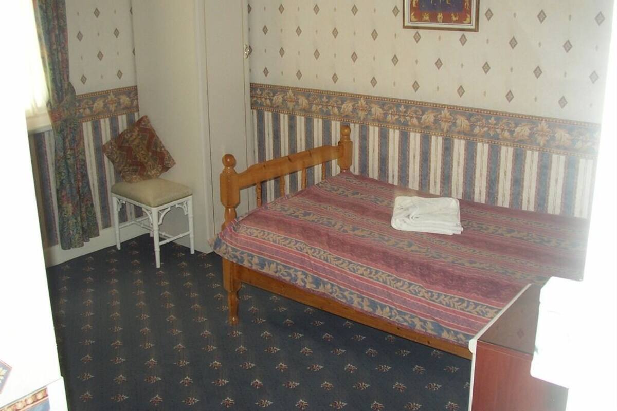 A room with a single bed, a chair, and a patterned carpet.