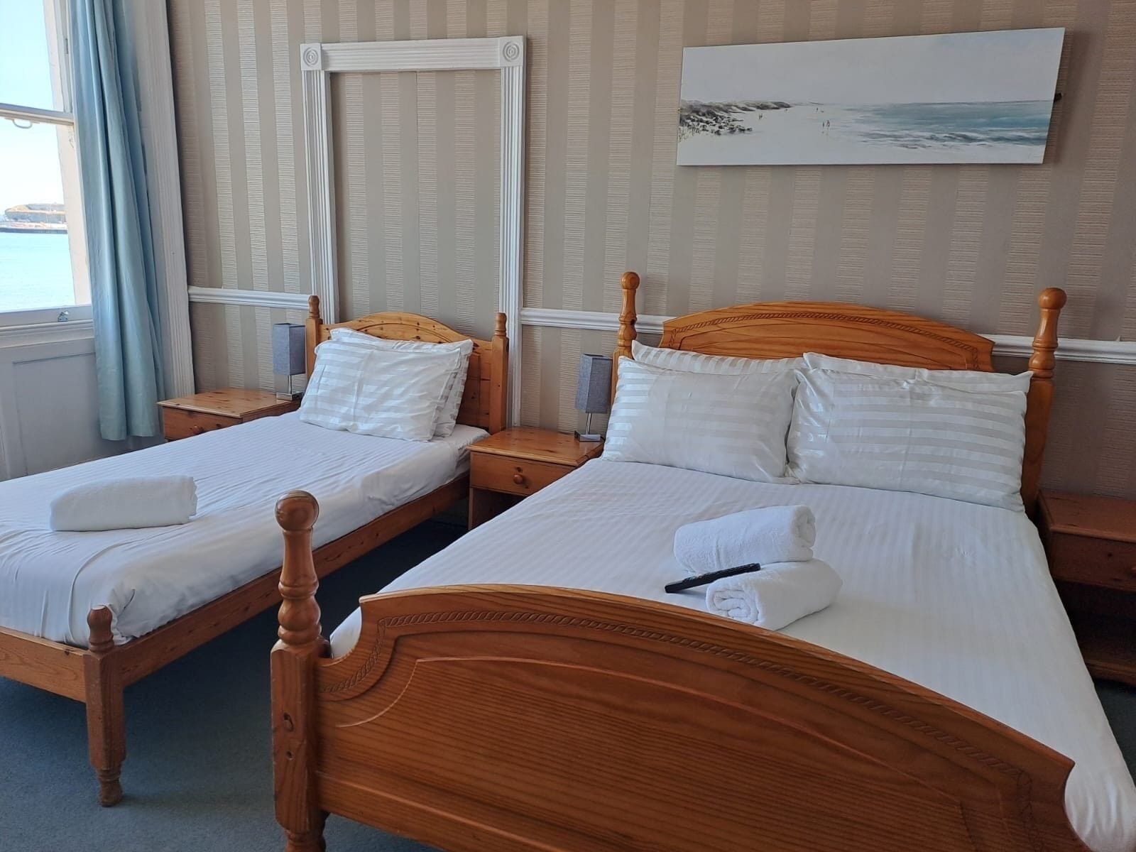 A hotel room with two wooden beds, white bedding, a painting on the wall, and a window with curtains.